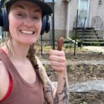 Woman with headphones and a brown tank top giving a thumbs up.